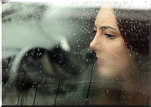 Sad woman looking out of a wet glass